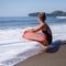 tanned surfer sitting with red surfboard on beach