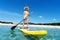 Tanned tourist female in straw hat standing on surfboard with paddle enjoying sup surfing