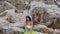 Tanned young woman in white bikini, sunglasses and big hat with mattress near the high rock by the sea. Summer vacation