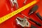 A tape measure, a screwdriver-tap, a flex-head wrench, and pliers lie on a red polished surface in a car repair shop. Mechanical