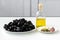 Tapenade ingredients: pitted black olives on white plate, olive oil in glass bottle, three cloves of garlic, some anchovy fillets