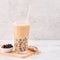 Tapioca pearl ball bubble milk tea, popular Taiwan drink, in drinking glass with straw on marble white table and wooden tray,