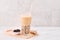 Tapioca pearl ball bubble milk tea, popular Taiwan drink, in drinking glass with straw on marble white table and wooden tray,