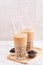 Tapioca pearl ball bubble milk tea, popular Taiwan drink, in drinking glass with straw on marble white table and wooden tray,