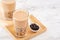 Tapioca pearl ball bubble milk tea, popular Taiwan drink, in drinking glass with straw on marble white table and wooden tray,