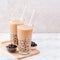 Tapioca pearl ball bubble milk tea, popular Taiwan drink, in drinking glass with straw on marble white table and wooden tray,