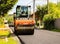 Targoviste, Romania - 2019. Close up photo of an orange road roller compacting the new asphalt with a dump truck and an asphalt