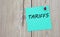 TARIFFS - word written on a green sheet for notes, which is pinned to a light wooden board
