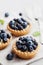 Tartlets with blueberries, bilberry, ricotta and honey syrup on gray vintage background. Delicious dessert.