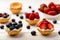 Tartlets with cream, blueberries, raspberries and strawberries on white wooden table. Selective focus.