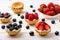 Tartlets with cream, blueberries, raspberries and strawberries on white wooden table. Selective focus.