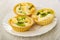 Tartlets with slices of kiwi, banana and yogurt in white plate on wooden table