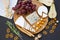 Tasting cheese with fruits, pretzels walnuts and bread sticks on dark background. Food for wine, romantic.