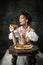 Tasting pizza. Vintage portrait of young beautiful girl in attire of medieval fashion style isolated on dark background