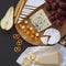 Tasting various types of cheeses with fruits, pretzels, walnuts and bread sticks on dark background. Food for wine. Overhead view,