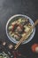 Tasty Asian food bowl with ramen noodles, meat balls, spices and chopsticks on dark background. Top view