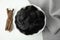 Tasty black candies and dried sticks of liquorice root on white table, flat lay