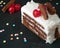 Tasty Black forest slice decorated with cherries and decorative and colorful sugar sprinkles on a black slate board. Close up View