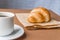 Tasty breackfast. French croissant served on craft paper and cup of black coffee or espresso on brown background. Banner