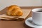 Tasty breackfast. French croissant served on craft paper and cup of black coffee or espresso on brown background. Copy space