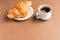 Tasty breackfast. French croissant served on white plate and cup of black coffee or espresso on brown background. Copy space