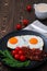 Tasty breakfast with fried eggs, crispy bacon, cherry tomatoes and arugula served on the black plate on the wooden table