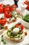 Tasty bruschettas with capers, vegetables and mozzarella served on white marble board, closeup