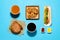 Tasty burger, hot dog, fried onion rings, different sauces and refreshing drinks on light blue background, flat lay. Fast food