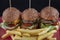 Tasty burgers, cheeseburgers, french fries, salad and red plaid kitchen textile, table top view. Three burgers or cheeseburgers,