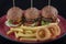 Tasty burgers, cheeseburgers, french fries, salad and red plaid kitchen textile, table top view. Three burgers or cheeseburgers,