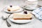 Tasty cheesecake with blackberry on a plate laying on a white wooden table with another cake and cup of coffee or tea on backgroun