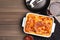 Tasty cooked lasagna in baking dish on wooden table, flat lay. Space for text