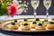 Tasty delicious tartlets with black caviar on a luxurious platter with two glasses of champagne and flowers