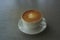 Tasty drinking, a cup of capuccino coffee decorated with heart pattern on brown milk froth in white ceramic cup on gray table