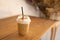 Tasty drinking, a cup of ice cappuccino coffee decorated with white milk froth in a tall plastic glass on brown wooden table