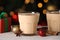 Tasty eggnog, cinnamon, anise and Christmas decorations on white wooden table against blurred lights