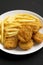 Tasty Fastfood: Chicken Nuggets and French Fries on a plate on a black background, low angle view. Close-up