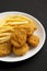 Tasty Fastfood: Chicken Nuggets and French Fries on a plate on a black background, side view. Close-up