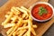 Tasty french fries on cutting board with sauce, on wooden table background