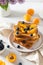 Tasty french toasts with blueberry, apricots and maple cyrup, a cup of coffee on the table with lilac bouquet. Trendy breakfast