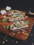 Tasty fresh bruschetta with mushrooms, spinach, garlic, cream cheese and pine nuts, on a wooden board, on a dark background.