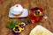 Tasty fresh cake on saucer, on wooden table. On table there is also cup with tea, pansy flowers and saucer with lemon