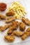 Tasty fried chicken drumsticks, spicy wings, French fries and chicken fingers with sour-sweet sauce on baking sheet over white woo