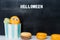 Tasty Halloween macaroons with funny face and eyes in paper cup on the black background with helloween message. Festive