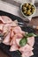 Tasty ham with basil, olives, peppercorns and carving fork on wooden table, flat lay
