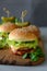 Tasty homemade burgers with lettuce, ketchup, cheese and chicken on gray wooden background. Copy space