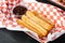 Tasty hot sweet churros in paper with chocolate and caramel in paper tray, on black wooden table background