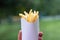 Tasty juicy french fries in white paper box in man hand on nature outdoors