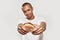 Tasty looking hamburger in hands of a dark-skinned tattooed man wearing white t-shirt, looking at camera and smiling on