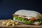Tasty panini burger with bacon, cheese, salad and chicken meat with potato on a wood platform on a blue paper background